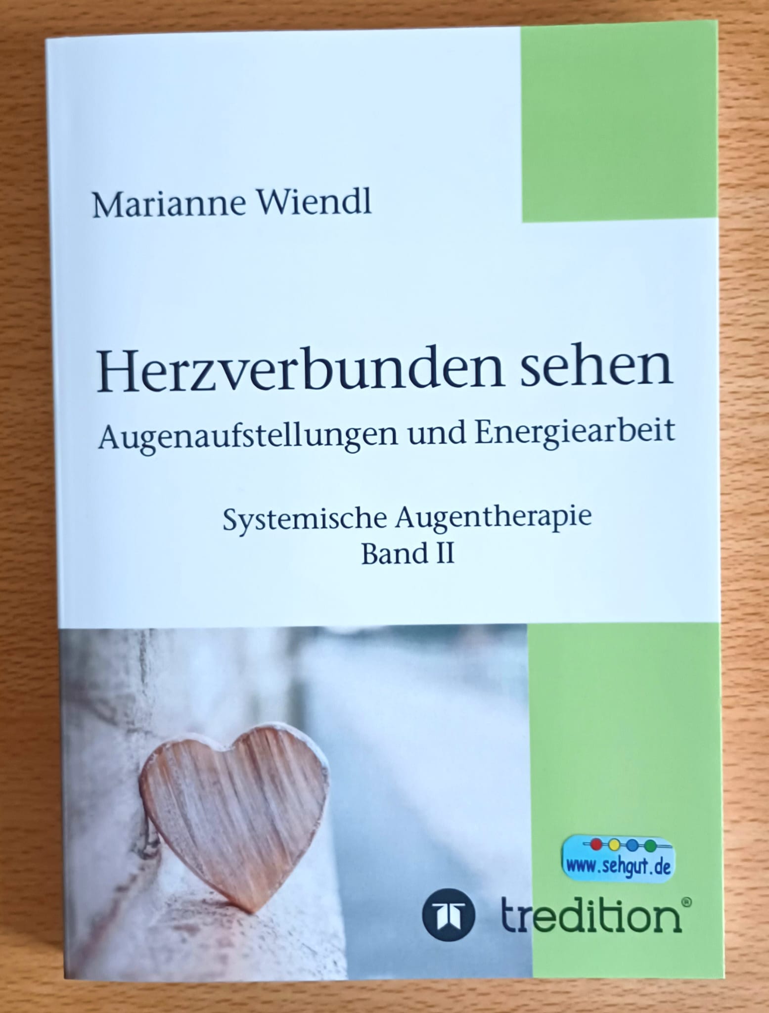 Das Buch "Herzverbunden sehen" ist weiß mit hellgrün und im Bild ist ein kleines Herz aus Holz zu sehen.