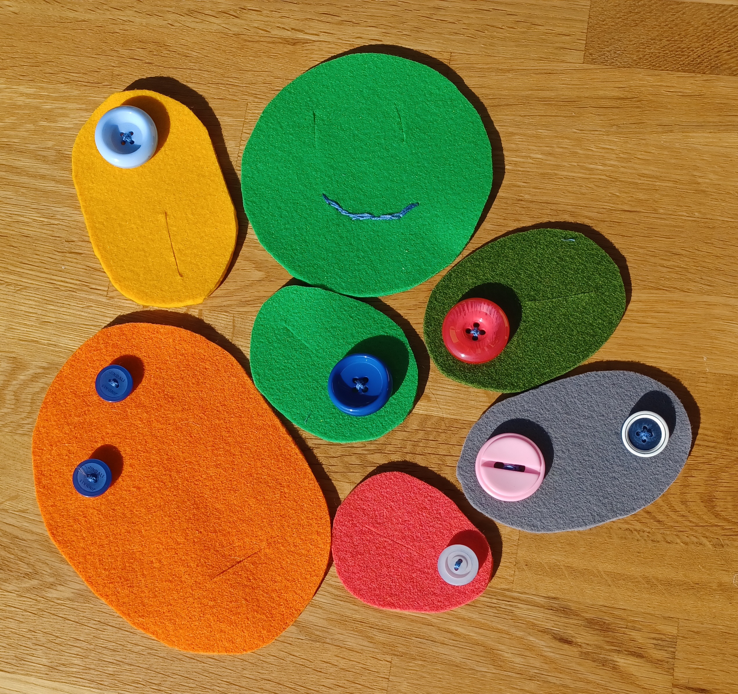 7 einfarbige Filzstücke mit einzelnen bunten Knöpfen benäht.