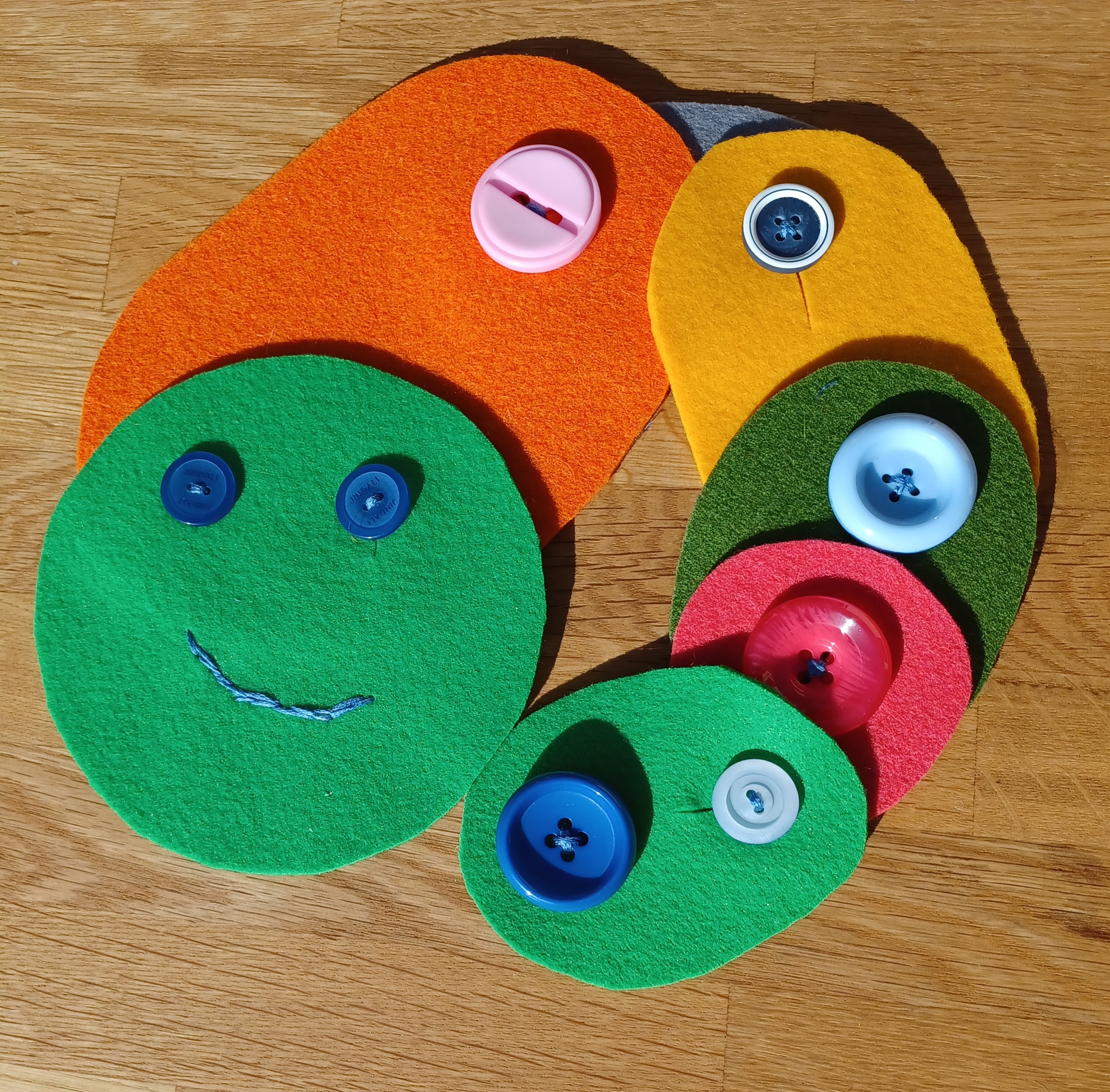 7 einfarbige Filzstücke mit einzelnen bunten Knöpfen benäht nun zusammengeknöpft.