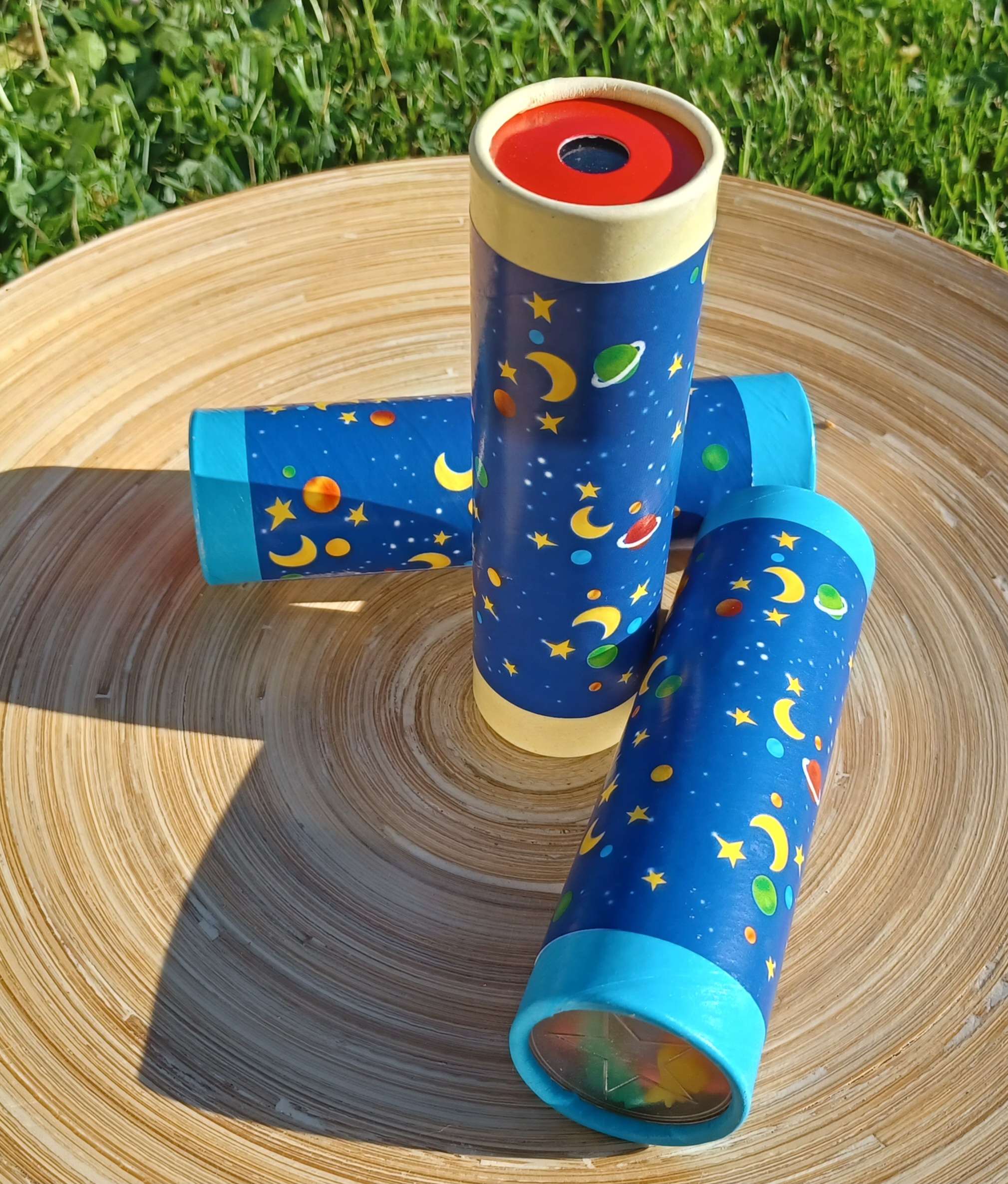 Drei Kaleidoskope liegen auf einem Holzteller im Sonnenschein.